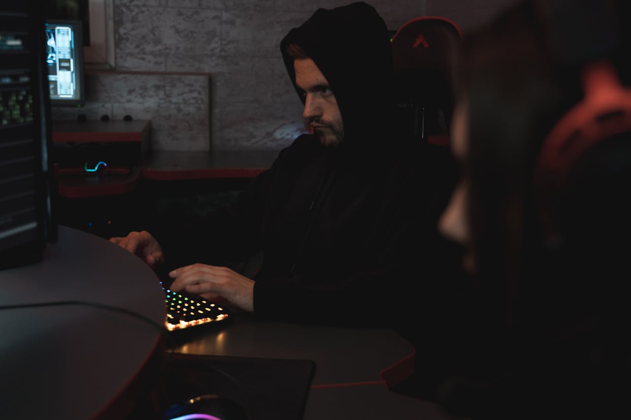 A man in a black hoodie works on a computer, focused on cyber security.